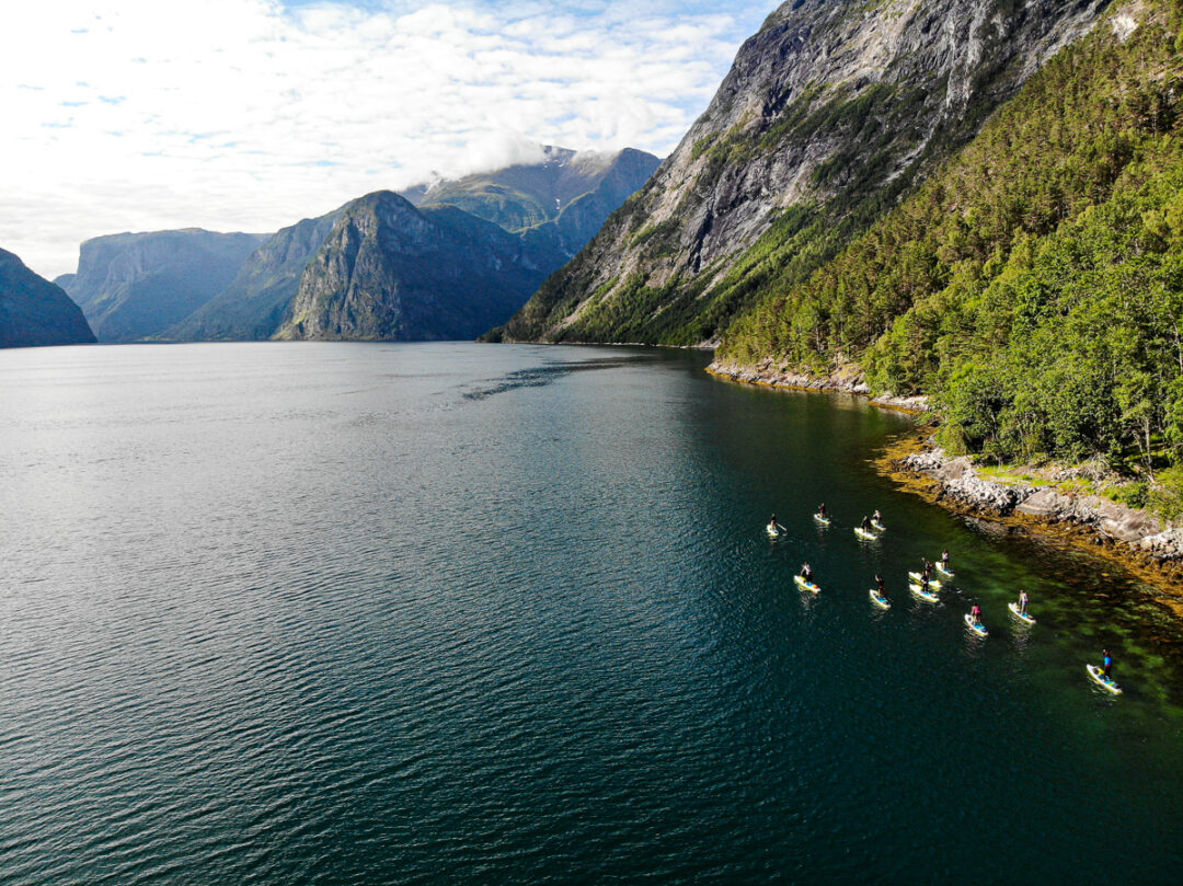 Kayakers on a calm fjord, paddling along steep mountain cliffs