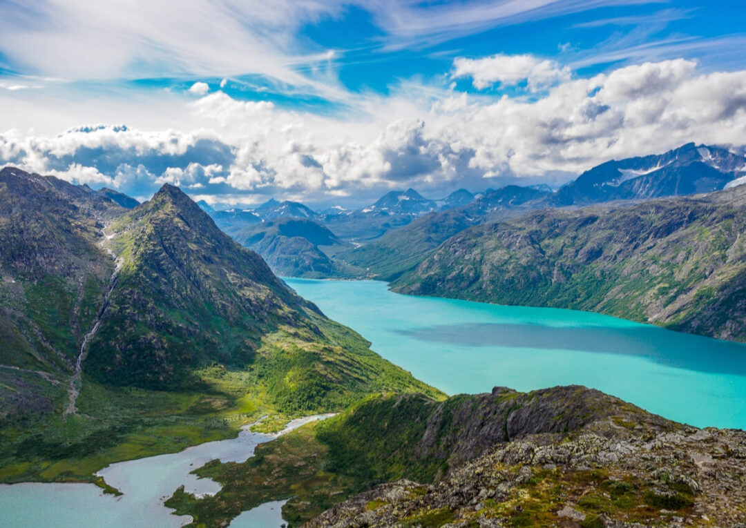 Turquoise glacier lake in a mountain valley, aerial landscape view over rugged peaks and forests