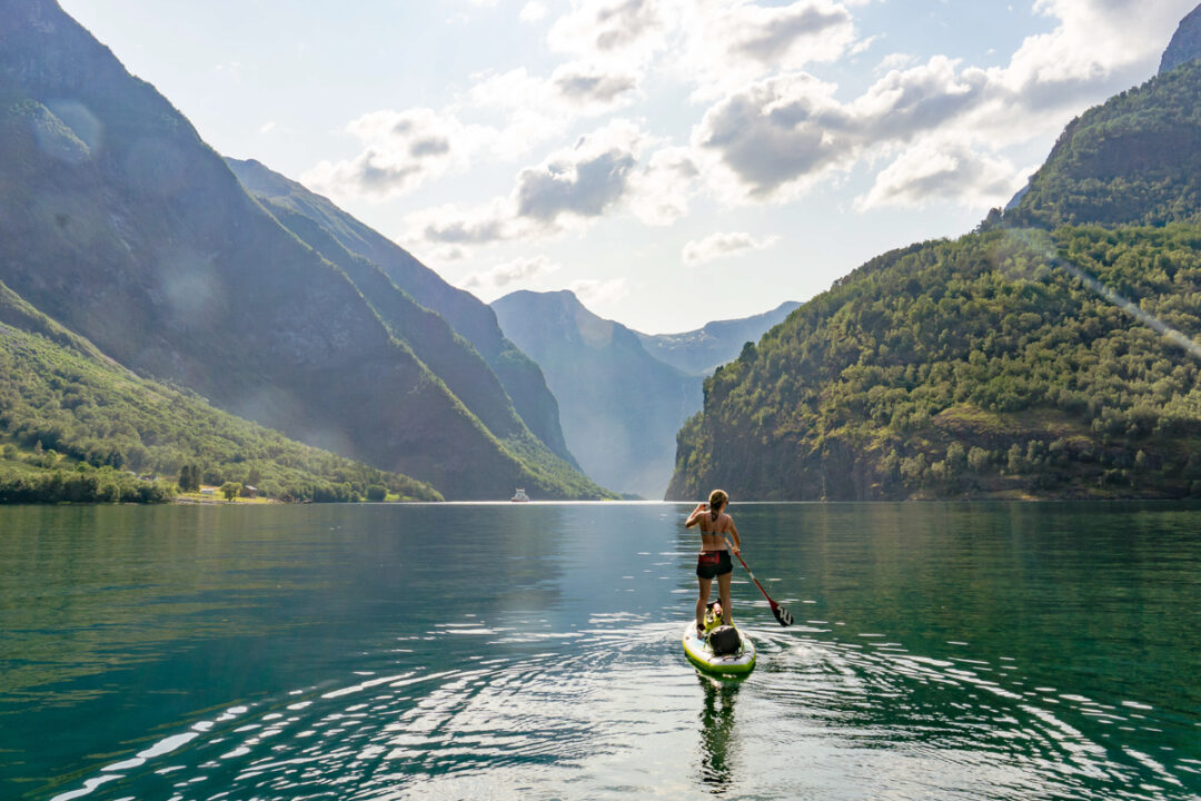 Person paddleboarding in serene fjord