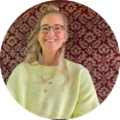Smiling woman with glasses sitting in front of a red patterned curtain background