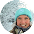 Smiling woman in winter gear and turquoise beanie outdoors in snowy forest with frosted branches