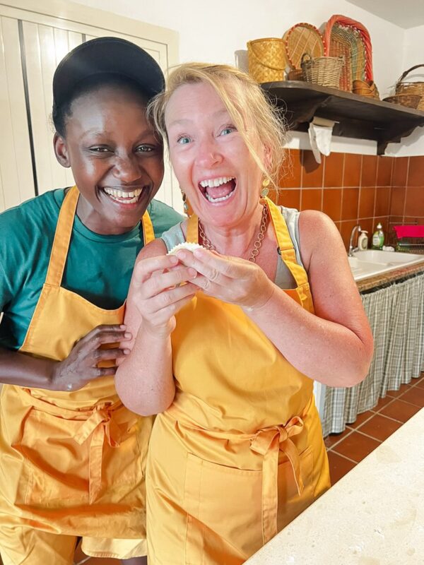 Two women in yellow aprons smiling and holding a small cake in a kitchen, Gutsy Girls adventure holiday.