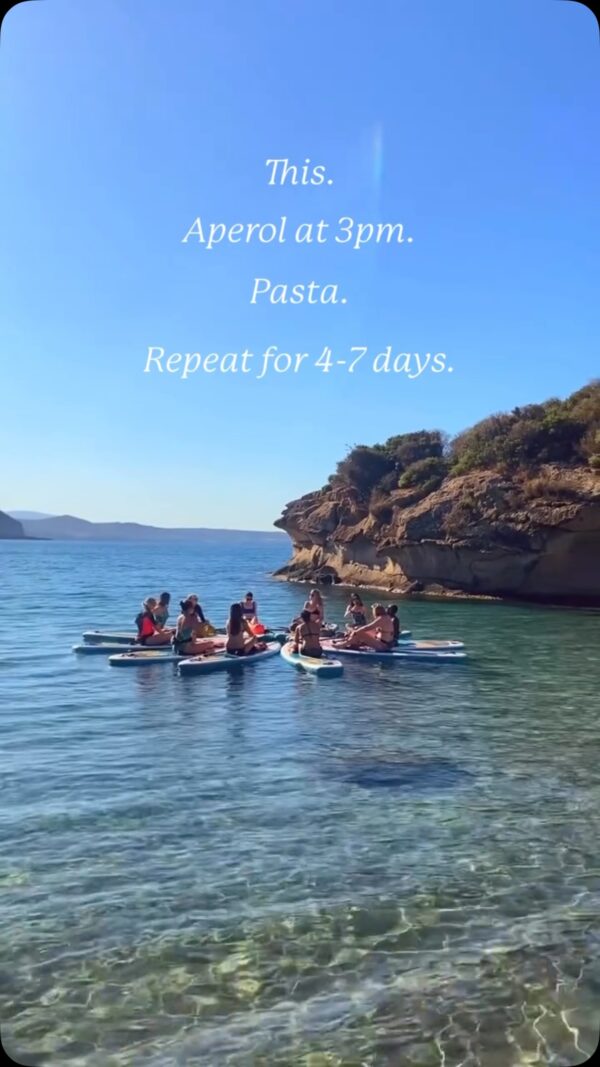 Women on paddleboards on clear sea by rocky coast; “This. Aperol at 3pm. Pasta. Repeat for 4–7 days.”