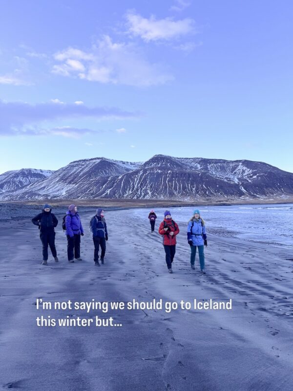 Women hiking on an icy beach in Iceland with mountains; “I’m not saying we should go to Iceland this winter but…”