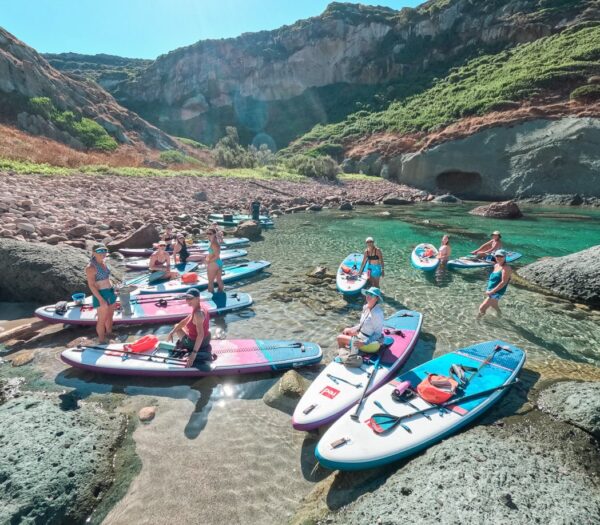 Women on stand-up paddleboards (SUP) in a rocky cove with mountains in Sardinia, Italy