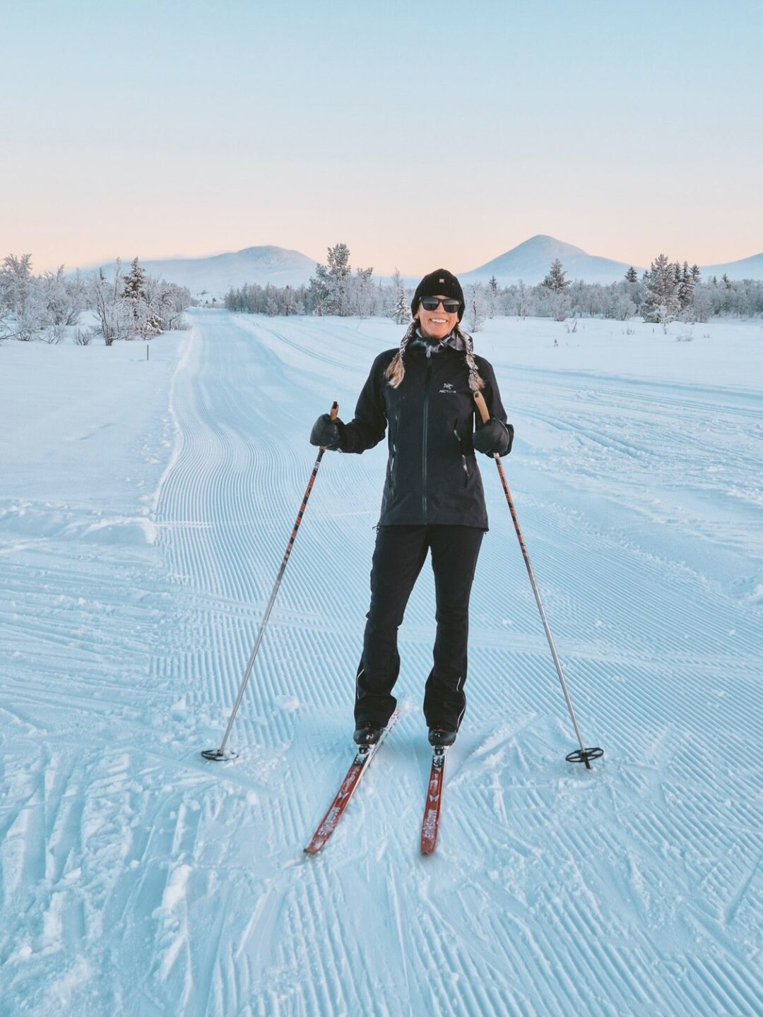 Woman cross-country skiing on snowy trails in Norway, gliding with skis and poles at dusk among snowy fells