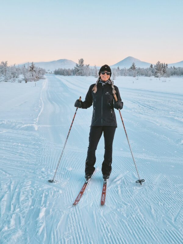 Woman cross-country skiing on snowy trails in Norway, gliding with skis and poles at dusk among snowy fells