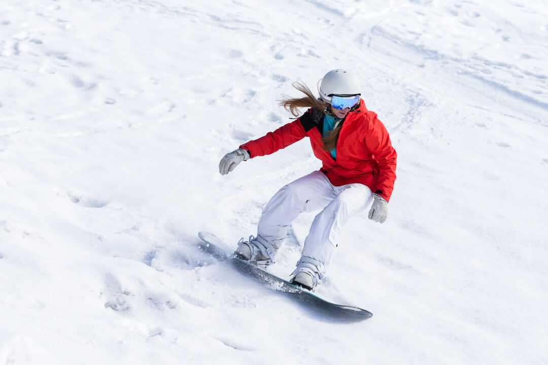 Woman snowboarding on a snowy slope, wearing a helmet and goggles in winter conditions