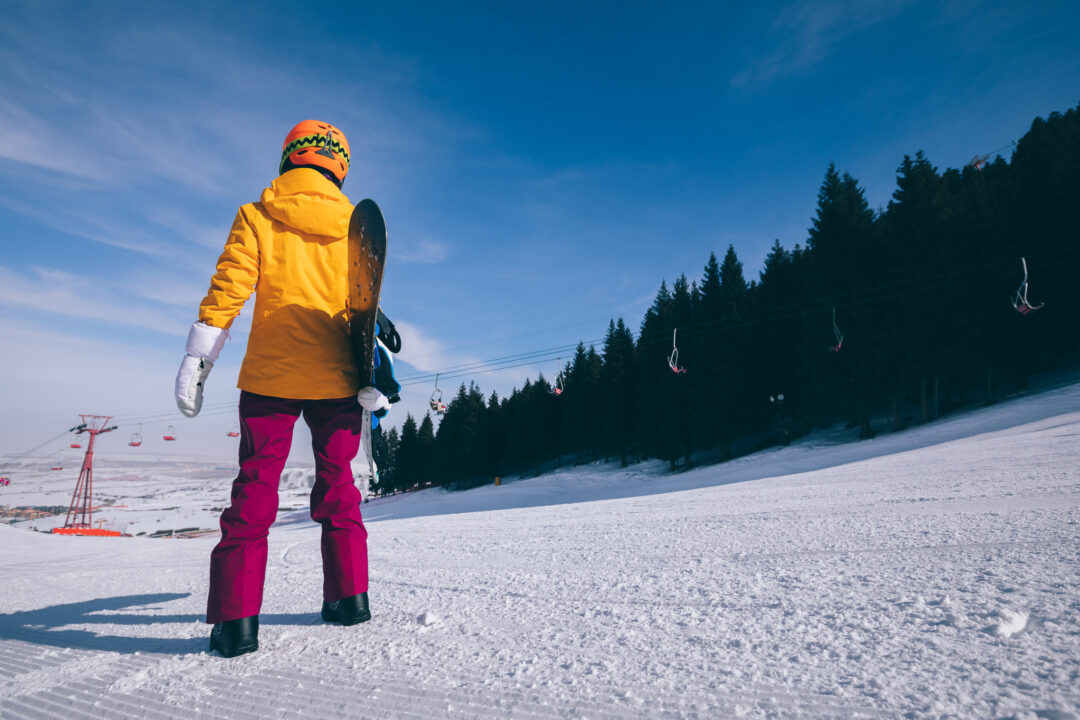 Woman snowboarder on a snowy ski slope with a chairlift and pine trees under a clear blue sky