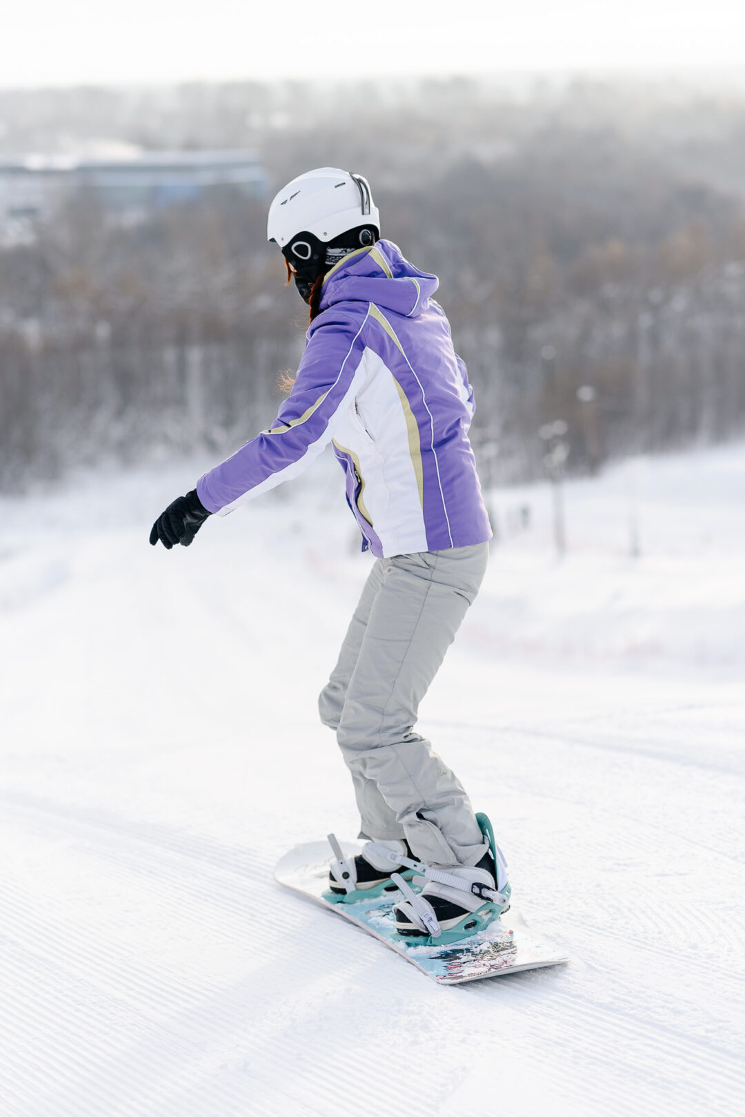 Woman snowboarding on a snowy slope, wearing a helmet and goggles in a mountain winter landscape