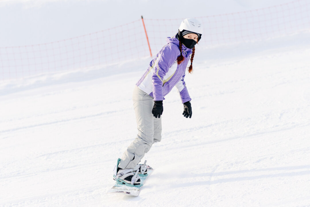 Woman snowboarding on a snowy slope, wearing a helmet, goggles and winter ski gear