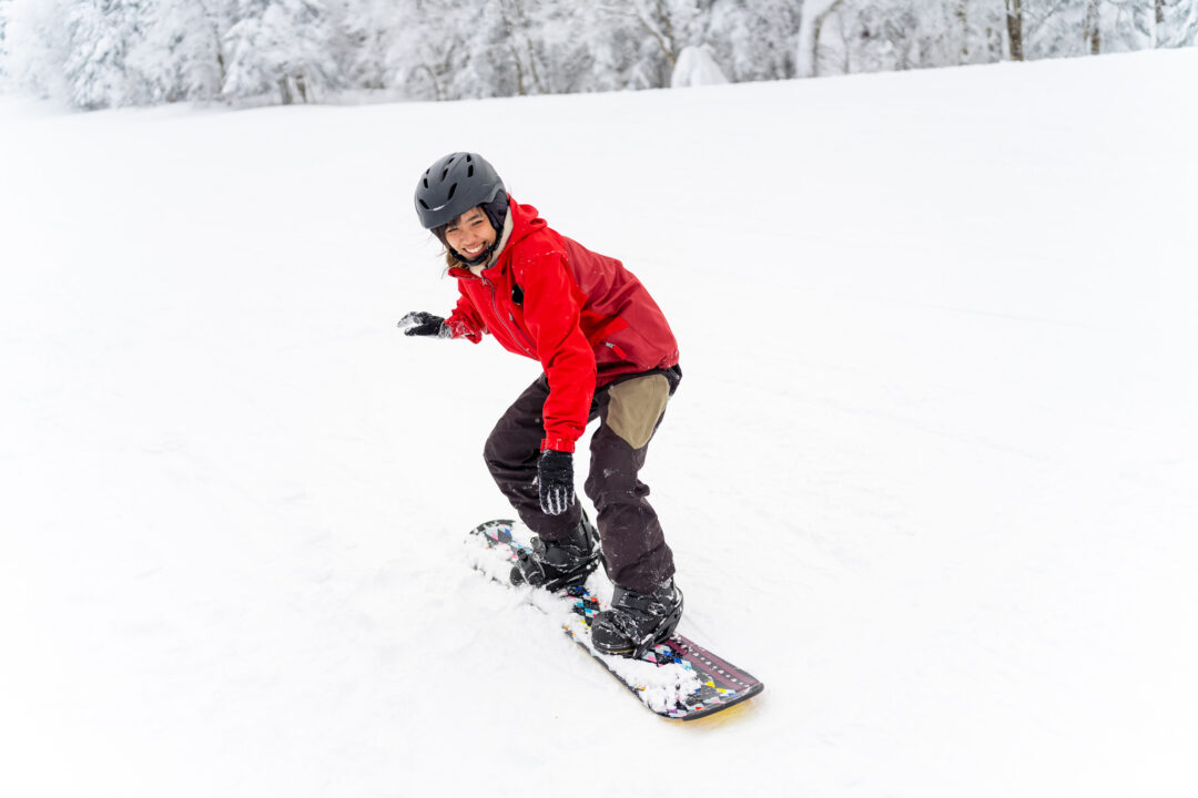 Woman snowboarding on a snowy piste in Norway, wearing a helmet and red jacket