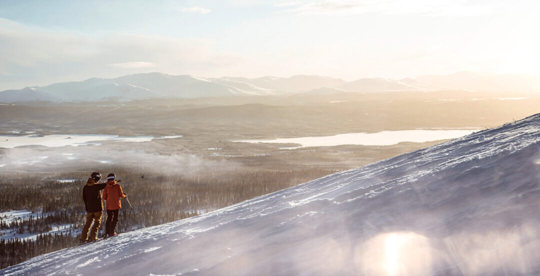 Two women skiing on a snowy slope at sunrise with wide mountain views