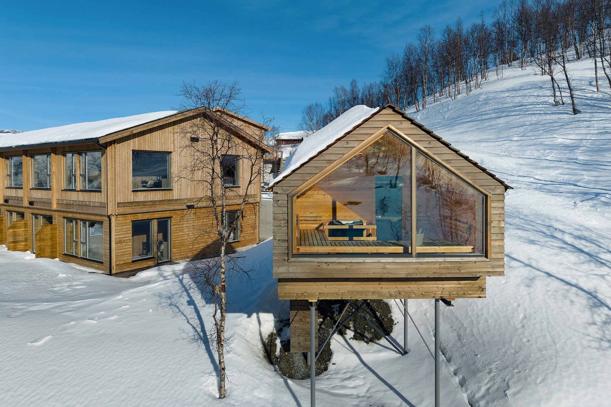 Wooden holiday cabins and snowy hillside in Norway, with bright blue winter sky and fresh snowdrifts