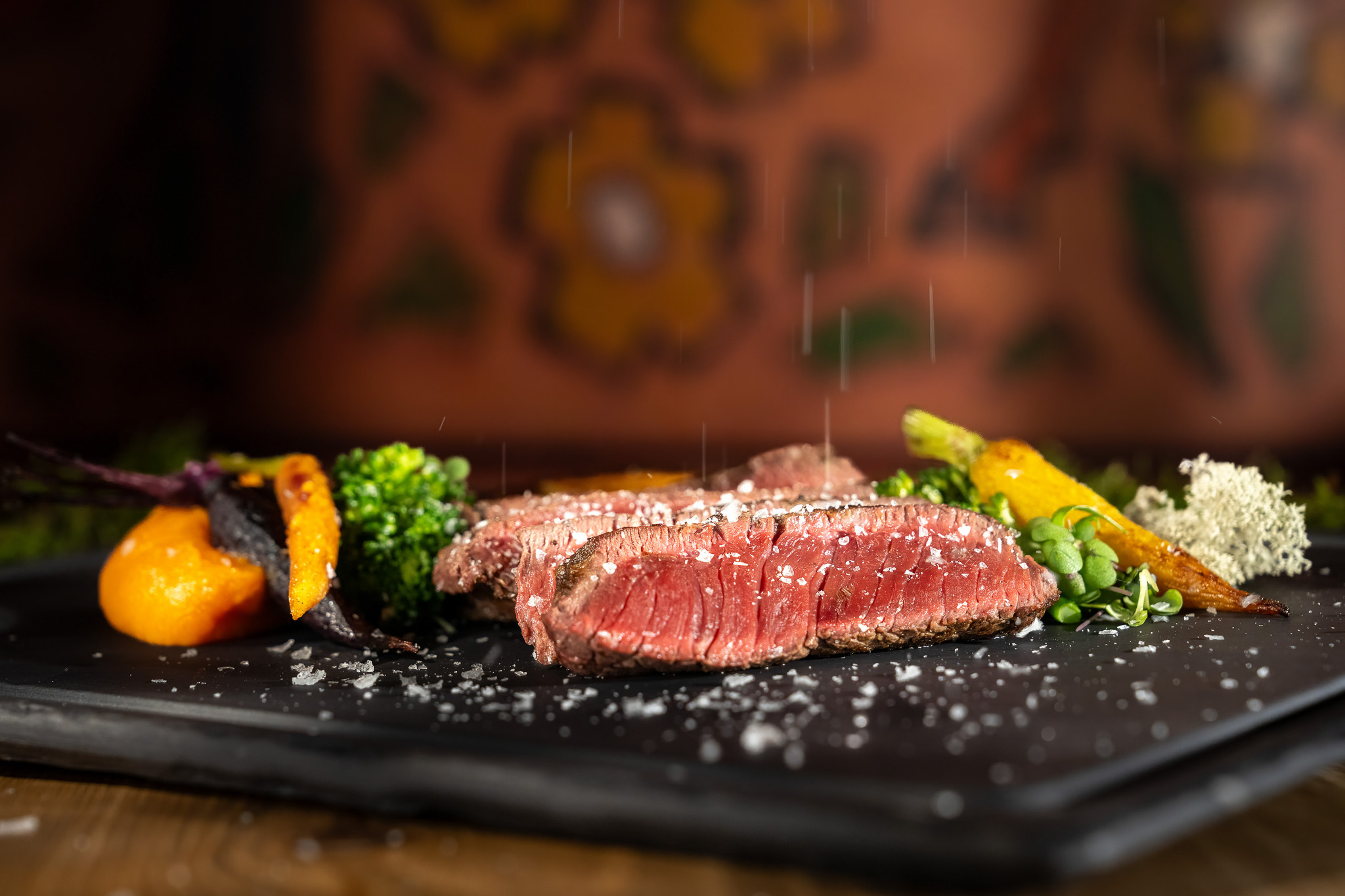 Seared steak on a platter with colourful vegetables, with water droplets in the air