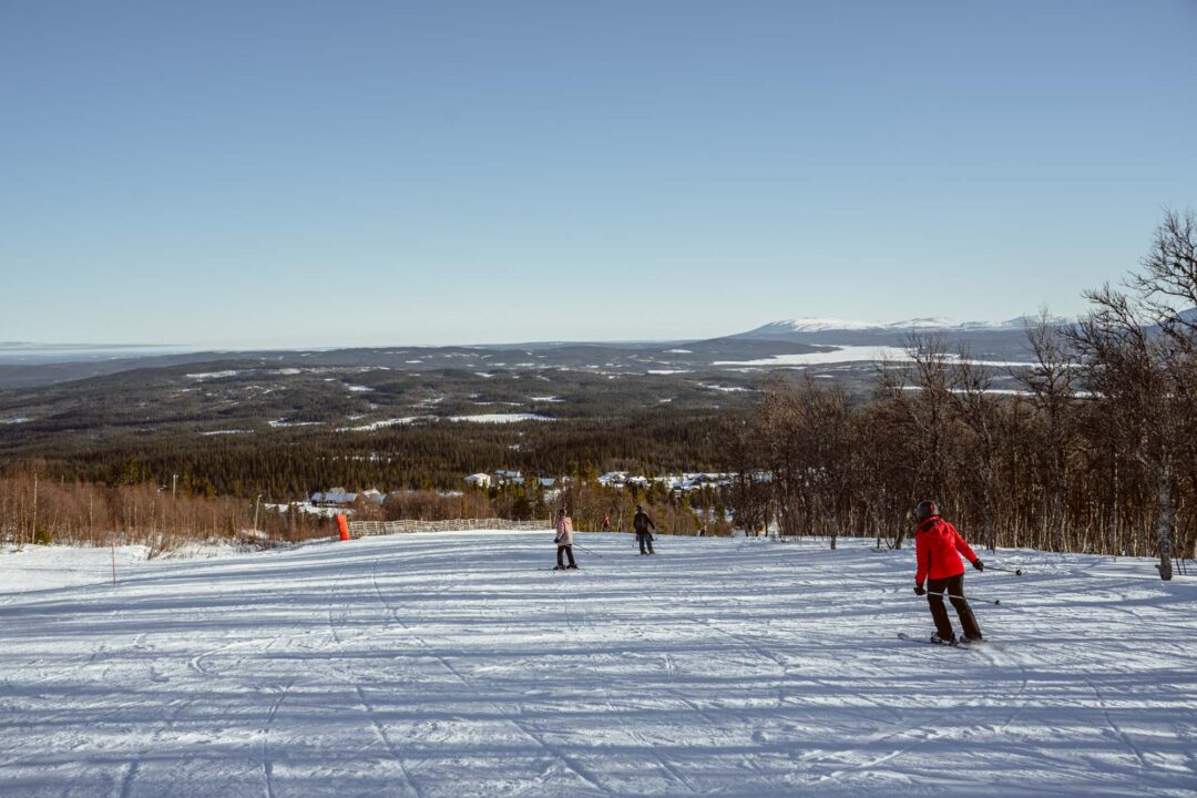 Skiers on a snowy slope overlooking a wide valley and distant mountains in winter