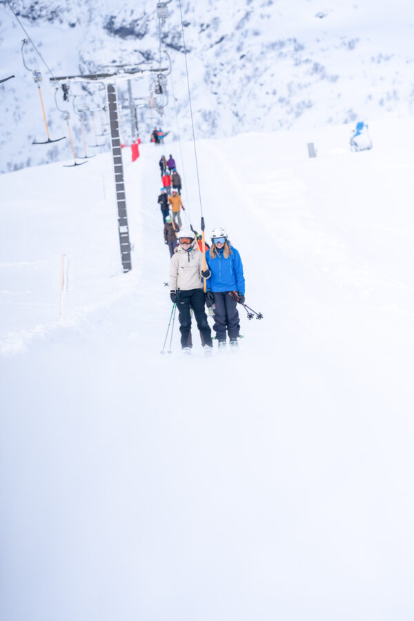 Women skiing on a chairlift in snowy mountains, with ski gear and skis visible