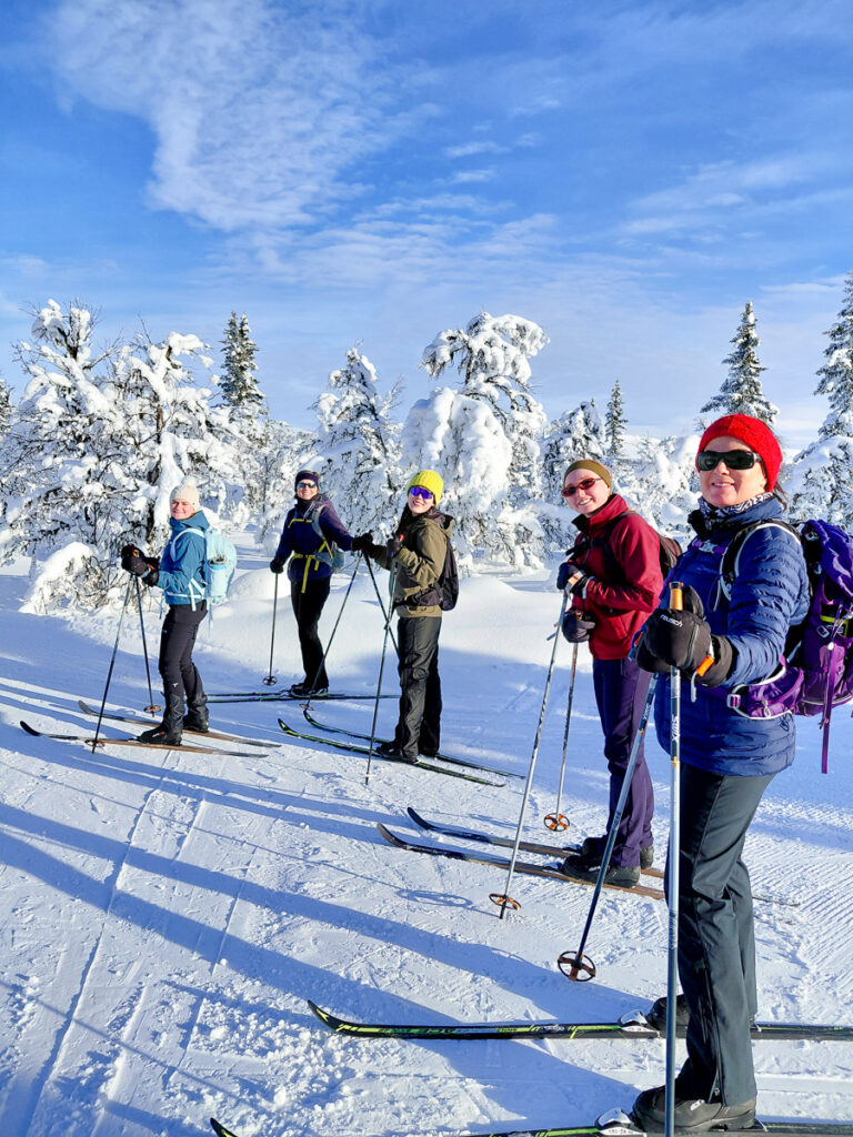 Women cross-country skiing in snowy Norway mountains with ski poles, standing on a groomed trail.